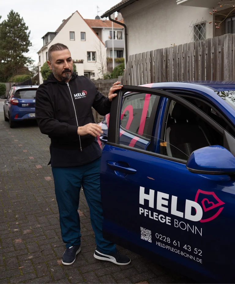 Pflegemitarbeiter von Held Pflege Bonn vor dem Firmenfahrzeug bei einem Außeneinsatz.