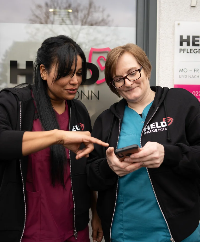 Pflegekolleginnen von Held Pflege Bonn besprechen Einsatzdetails am Smartphone.
